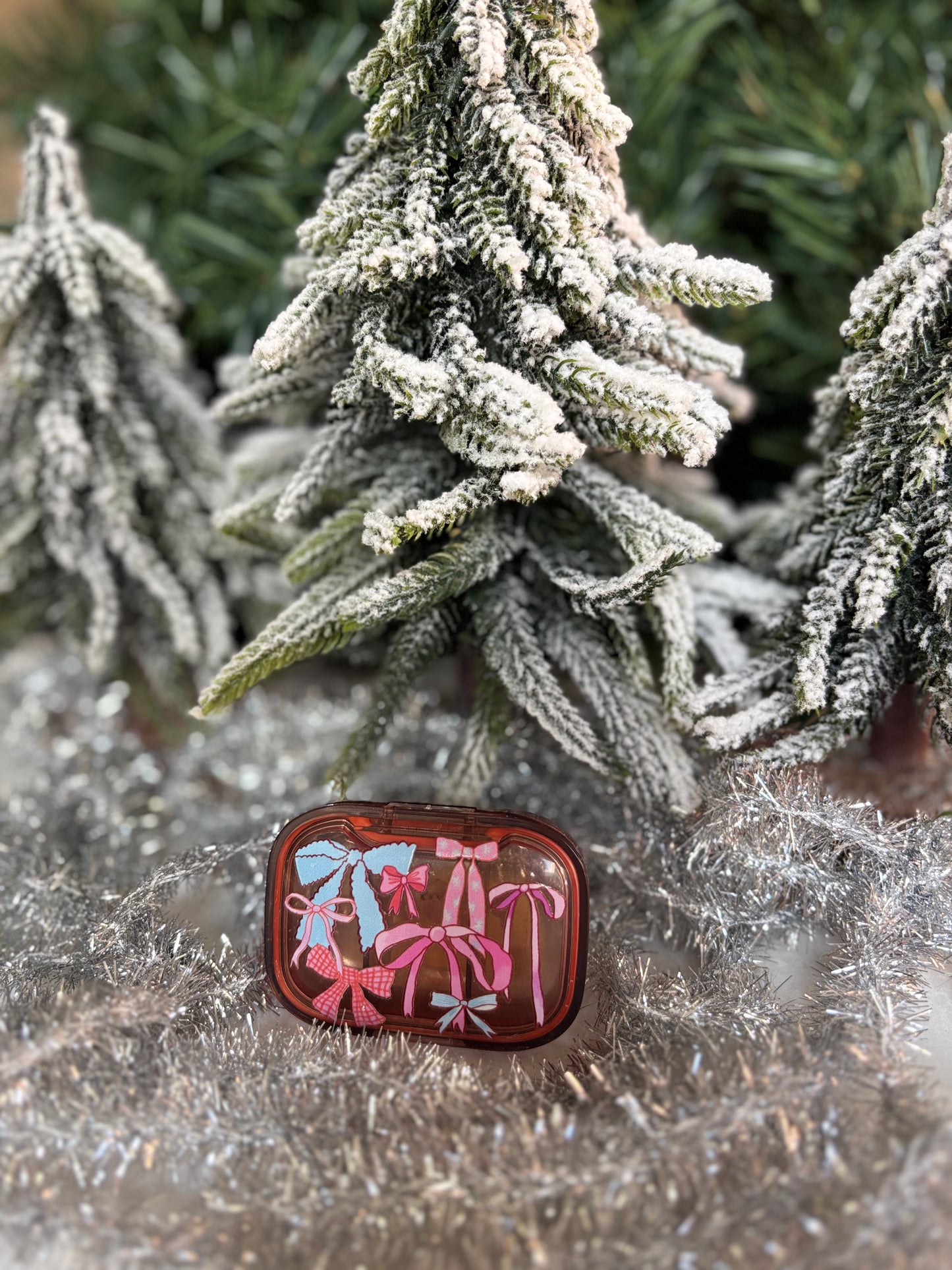 Peach pill pot with decorative ice blue and pink bows, set in front of minature christmas tree and silver tinsel