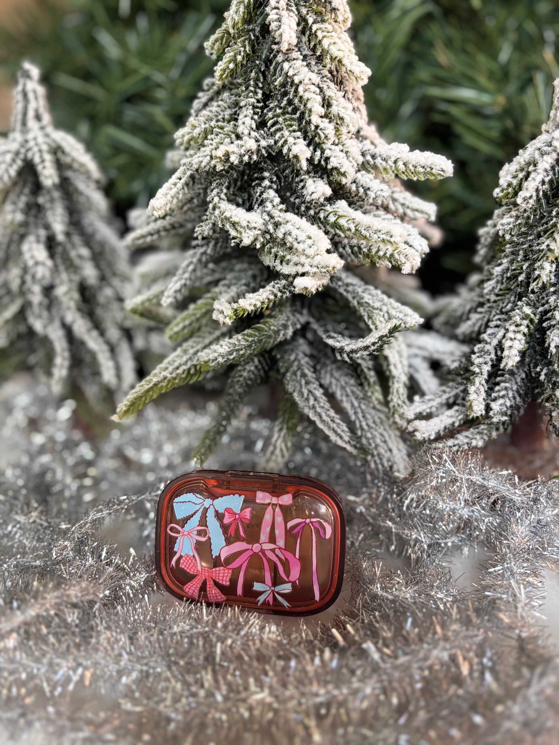 Peach pill pot with decorative ice blue and pink bows, set in front of minature christmas tree and silver tinsel
