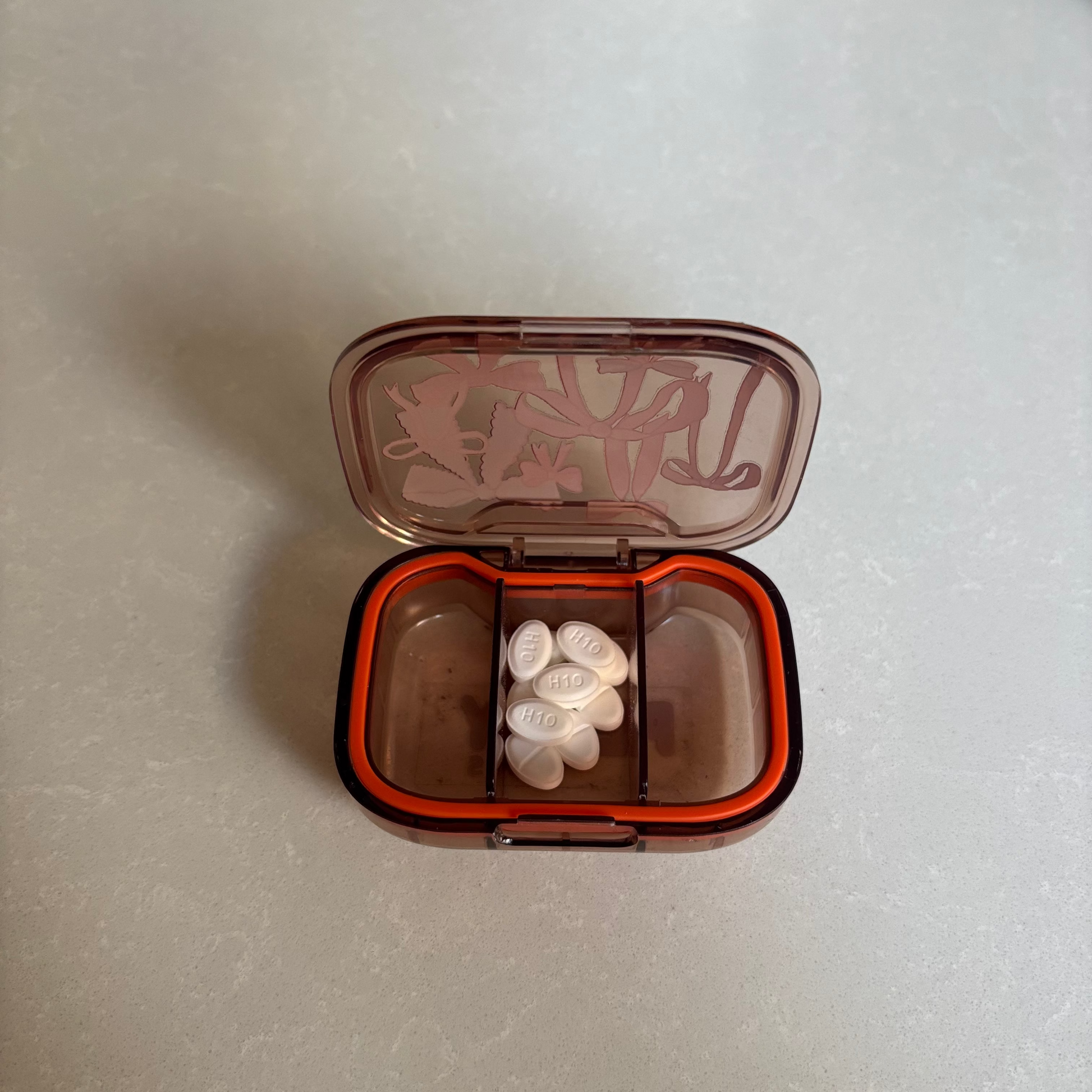 Small open pill  pot showing tablets in the middle of 3 compartments on a white surface